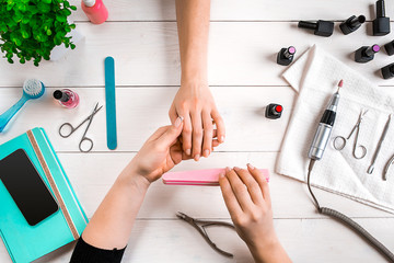 Manicure for the client. Close-up of the hands of a manicurist and client on a wooden background