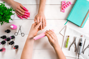 Manicure for the client. Close-up of the hands of a manicurist and client on a wooden background