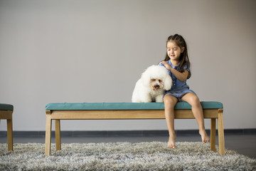 Little girl playing with white poodle in the room