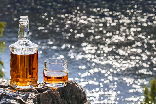Bottle and a glass of whiskey on a rock above the river