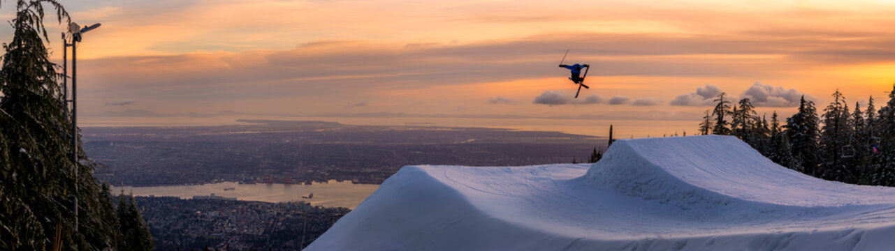 Freestyle skier doing a trick off a jump above city at sunset, Canada
