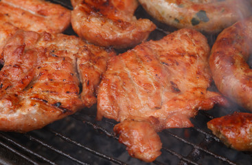 Grilled pork cooking with smoke on flaming grill.