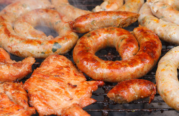 Grilled sausage and pork cooking with smoke on flaming grill.