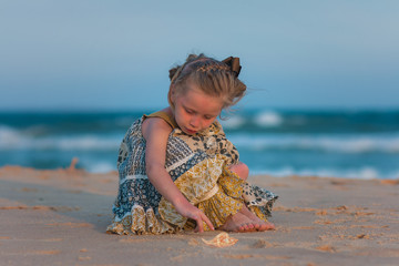 Kids lifestyle outdoor. Happy cute gir playing with sand on the beach of sea. Summer vacation and family travel concept.