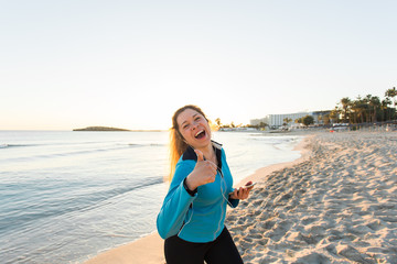 Motivated sporty woman doing thumbs up success gesture after urban workout on seashore.