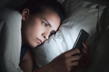 Donna usa smartphone a letto, gelosia o insonnia 
