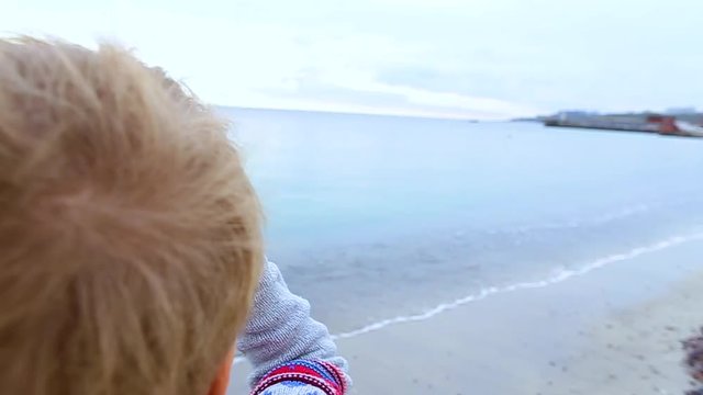 Little child looks through old telescope at something interesting in blue sea. Happy 8 year old kid has fun on beach on vacation in cool spring or autumn season. Real time hd video footage.
