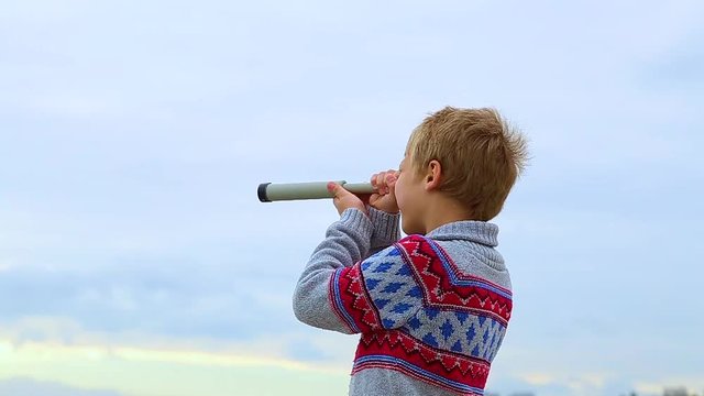 Little child looks through old telescope at something interesting in blue sea. Happy 8 year old kid has fun on beach on vacation in cool spring or autumn season. Real time hd video footage.