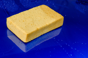 Handheld yellow sponge using for car washing and water droplet on the surface of blue car