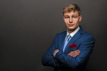 Young handsome man in blue suit smiling on dark background