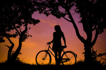 A young woman is standing with bicycle, resting, with the night sky background