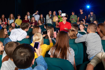 Group of kids taking pictures of their friend while he is wearing virtual reality goggles headset...