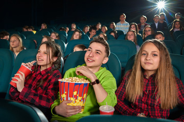 Beautiful young girls smiling to the camera while watching a movie at the cinema with her friends...