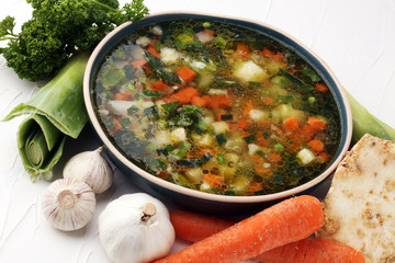 Broth with carrots, onions various fresh vegetables in a pot - colorful fresh clear spring soup. Rural kitchen scenery vegetarian bouillon or stock