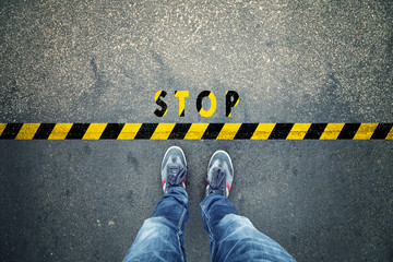 Top view of a man stands on industrial striped asphalt floor in front warning yellow black pattern and stop sign. - obrazy, fototapety, plakaty