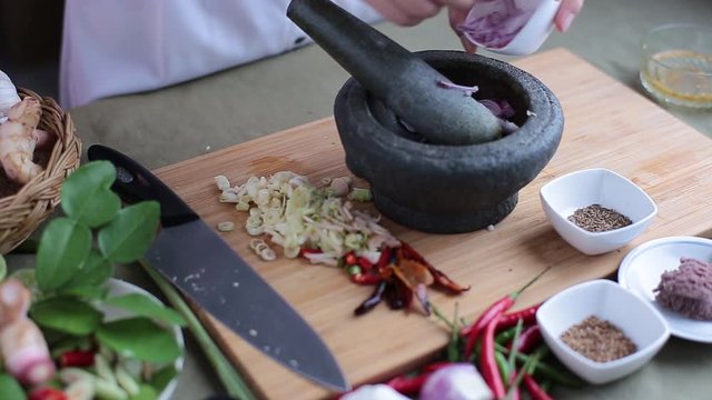 A female hand put many kinds of Thai herbs in mortar and pulverize to make Thai red curry chili paste or Panang.