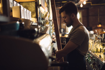 Obraz na płótnie Canvas Young male barista preparing drink at coffee machine