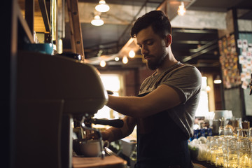 Young male barista preparing drink at coffee machine