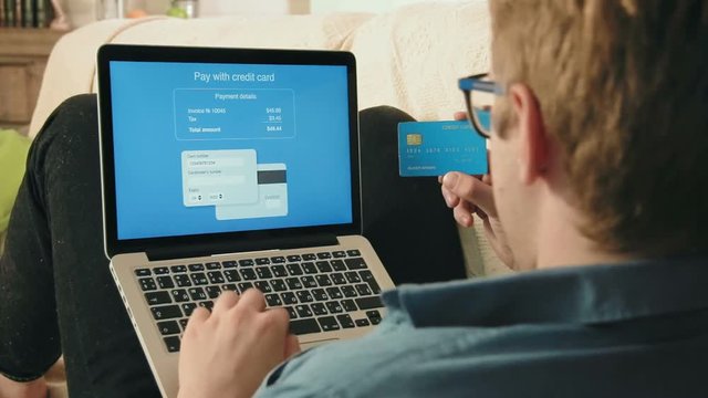 Young man filling credit card number on his laptop computer paying for online shopping