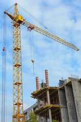 Yellow construction cranes and unfinished building with metal-concrete structure on a background of blue sky with white clouds.