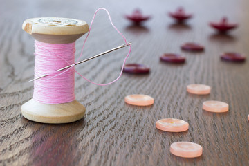 Spool pink thread with a needle. Pink and claret buttons on the table