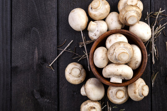 Fresh white mushrooms champignon in brown bowl on dark wooden background. Top view. Copy space.