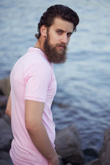 Portrait of a young and handsome  man with a beard in trendy t-short posing on the sea shore. Close up. Sea/beach fashion concept.