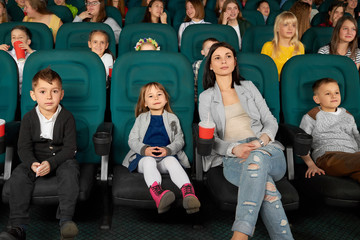 Full length shot of a beautiful young woman smiling watching a movie with her kids at the local cinema entertainment family parenting motherhood kids mother parent leisure activity happiness concept.