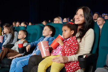 Fototapeta premium Young beautiful woman smiling holding her young daughter on the lap enjoying movie premiere at the cinema copyspace happiness living people leisure activity weekend togetherness concept.