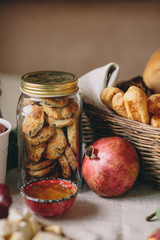 A glass jar with biscuits and cookie, a wicker basket with bread, pomegranate