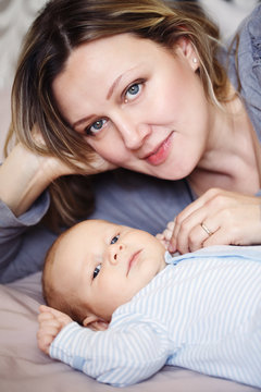 Closeup portrait of beautiful white Caucasian woman mother and cute adorable newborn baby lying on bed together looking in camera