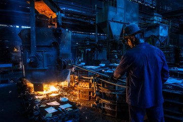 Foundry worker pouring hot metal into cast. Molten metal. Left over material from the steel...