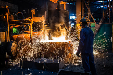 Foundry worker pouring hot metal into cast. Molten metal. Left over material from the steel manufacturing process is poured away on at a Steel Foundry