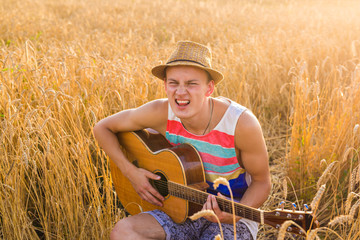 Naklejka na ściany i meble Young man playing guitar in the field on sunset