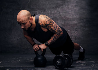 Shaved head sporty male doing push ups on Kettlebell.