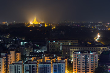Apartment buildings and lit Shwedagon Pagoda in Yangon, Myanmar, viewed from above in the evening.