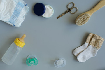 Set of accessories for baby. Pacifier, bottle, comb, socks, diaper, cream, scissors on grey background.maternal concept
