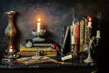 Classic still life with vintage books placed with illuminated candles,pocket watch,pipe,glasses and old copper vase on marble background 