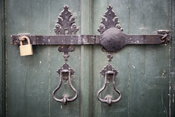 ancient door knockers, a metallic bar and a padlock on an ancient green wooden door
