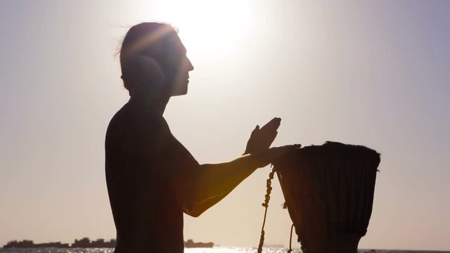 Drum Jembe playing. Drummer. Male Silhouette with Jembe near Sea.