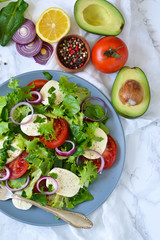 Vegetable salad with tomatoes, mozzarella and sauce on a marble background.