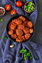 Homemade meatballs with tomato sauce and onions in a frying pan on a concrete background