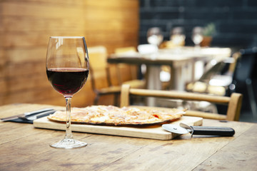 Traditional ham and brie cheese pizza with glass of red wine on rustic table