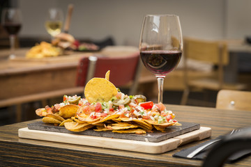 Traditional atmosphere with colorful plate of nachos flavored with vegetables and glass of red wine on rustic wooden table