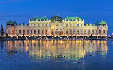 Upper Belvedere Palace with Christmas Village reflecting in the pond covered with wet ice in evening, Vienna, Austria - obrazy, fototapety, plakaty