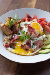 Eggs over medium with a side of avocado, bacon, potato, and tomato 