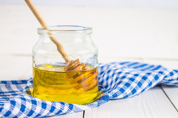 A honey jar with a spoon, on a white table with a blue towel.