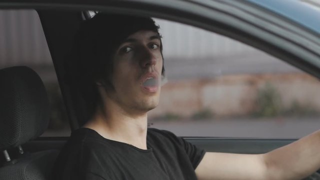 Man vaper makes smoke with electronic cigarette sitting in car.