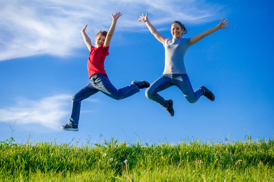 Two kids jumping on green hills against blue sky