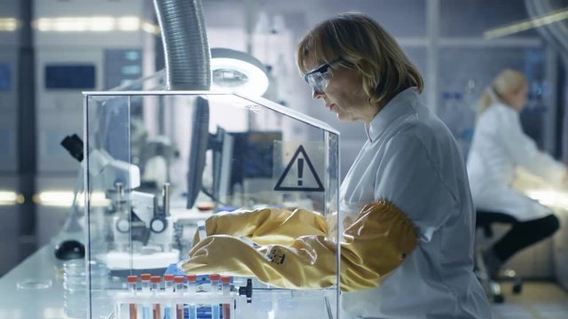 Senior Female Biologist Works with Samples in Isolation Glove Box. She's in a Modern, Busy Laboratory Equipped with State of the Art Technology. Shot on RED EPIC-W 8K Helium Cinema Camera.